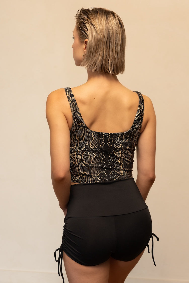Woman wearing a snakeskin pattern top and black shorts on a beige background