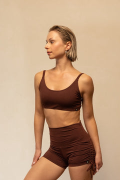 Woman wearing a brown sports bra and shorts set against a beige background